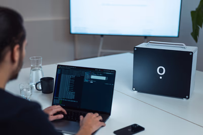 Entwickler arbeitet am Laptop mit Terminalansicht, daneben steht die Airene-KI-Box als lokale On-Premise-Hardware.