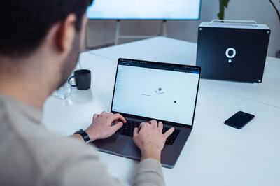 Mitarbeiter nutzt am Laptop die Airene-Weboberfläche, im Hintergrund steht die lokale Airene-KI-Box im Besprechungsraum.