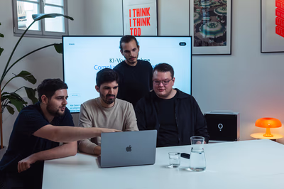Das IOWIS-Team sitzt gemeinsam am Tisch und arbeitet an einem Laptop, im Hintergrund ist auf einem großen Bildschirm die IOWIS-Website mit Airene zu sehen.